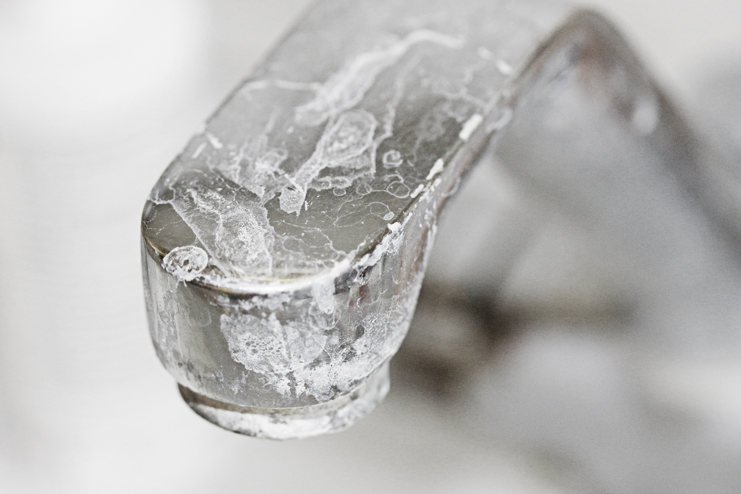 A close-up of a metallic faucet covered in white mineral deposits and limescale buildup, showing hard water stains and lack of cleaning—issues that can be prevented with water softeners. The background is blurred.